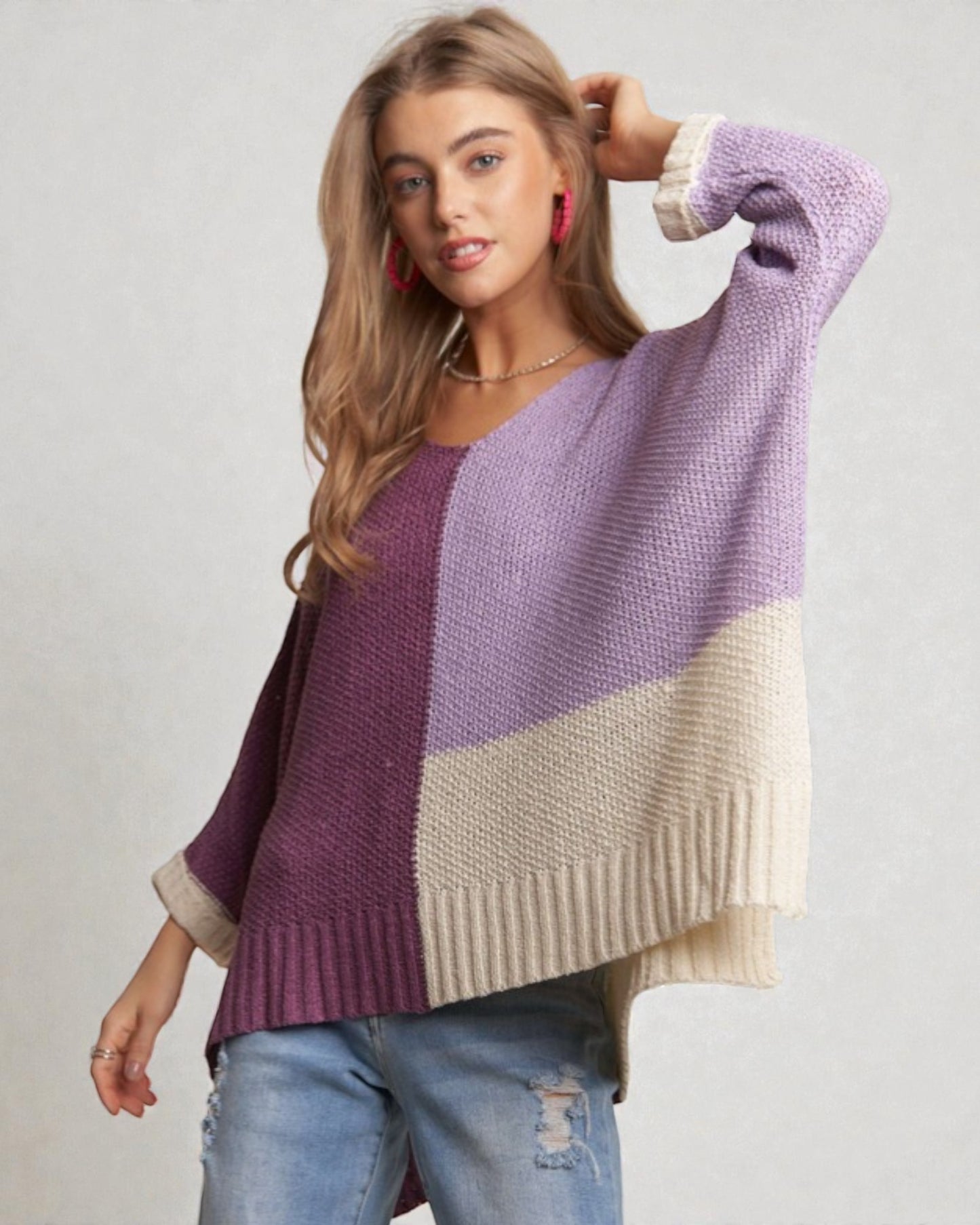 Woman wearing a color-blocked sweater with purple, beige, and white sections on a plain background.