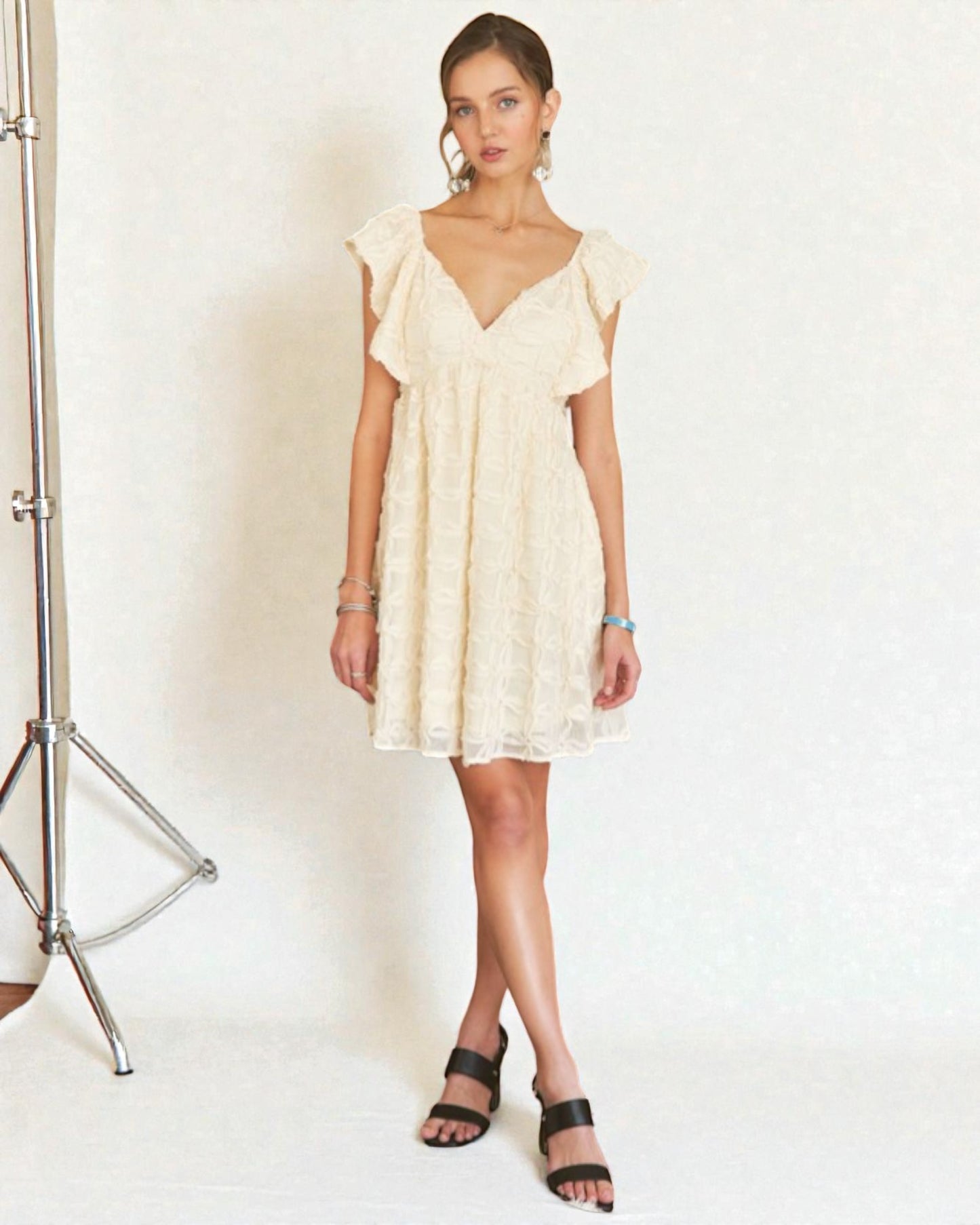 Woman wearing a light-colored dress with ruffled sleeves against a white background