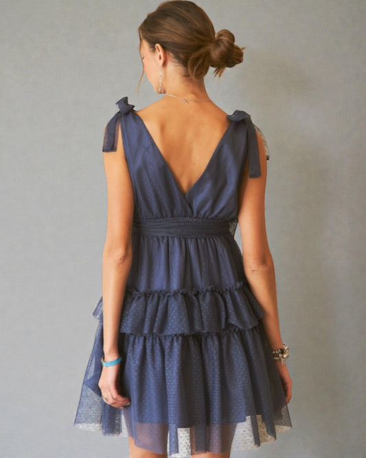 Woman wearing a navy blue dress with ruffled layers on a plain background