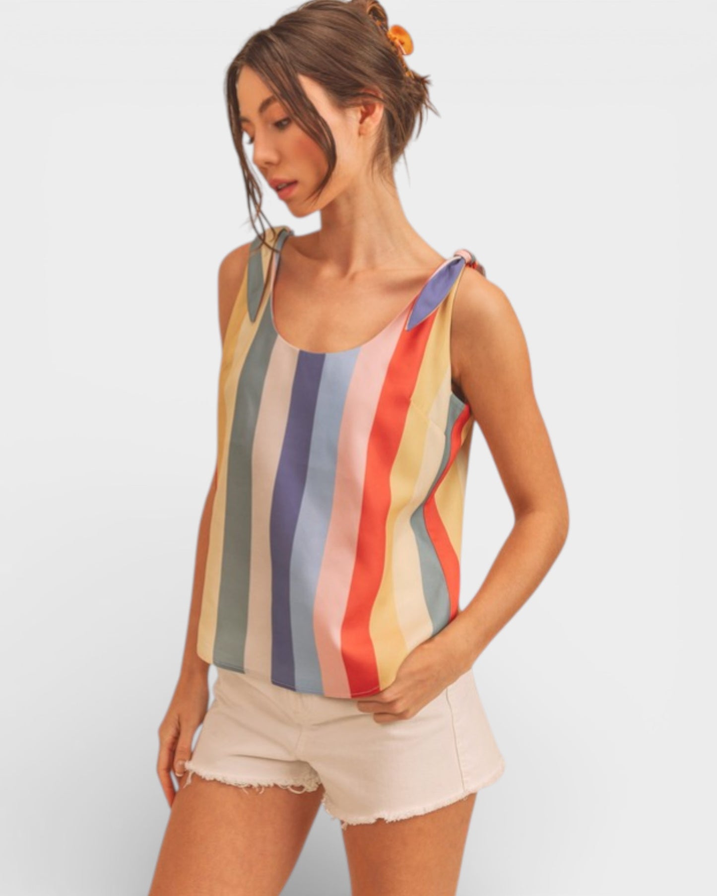 Woman wearing a colorful striped tank top and white shorts on a plain background