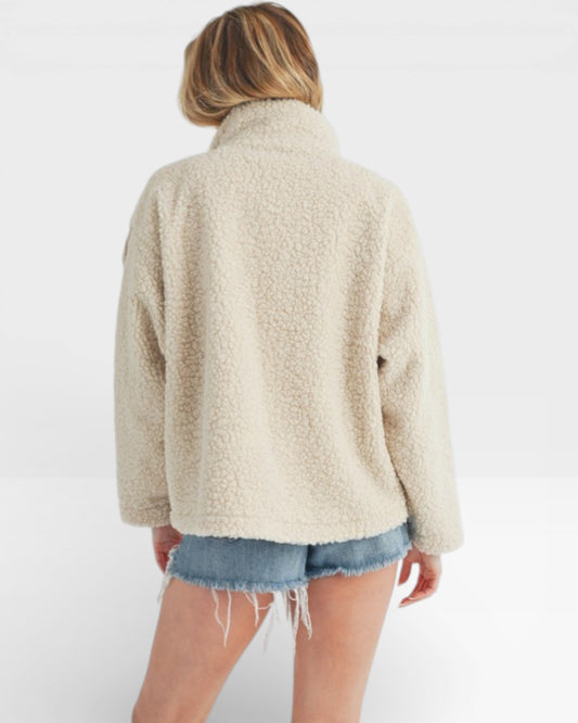 Person wearing a beige fleece jacket and denim shorts on a white background