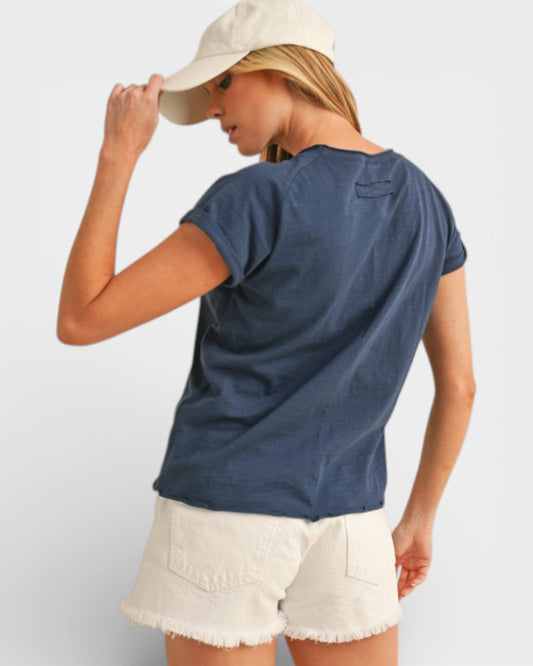 Woman wearing a blue t-shirt and white shorts with a beige cap on a light gray background
