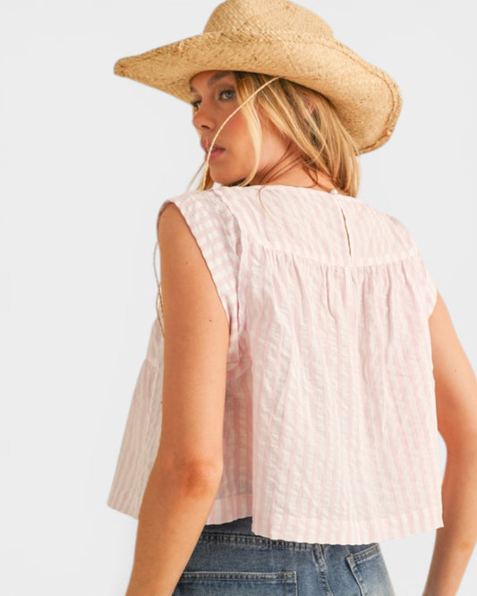 Woman wearing a sleeveless white top and straw hat on a light background