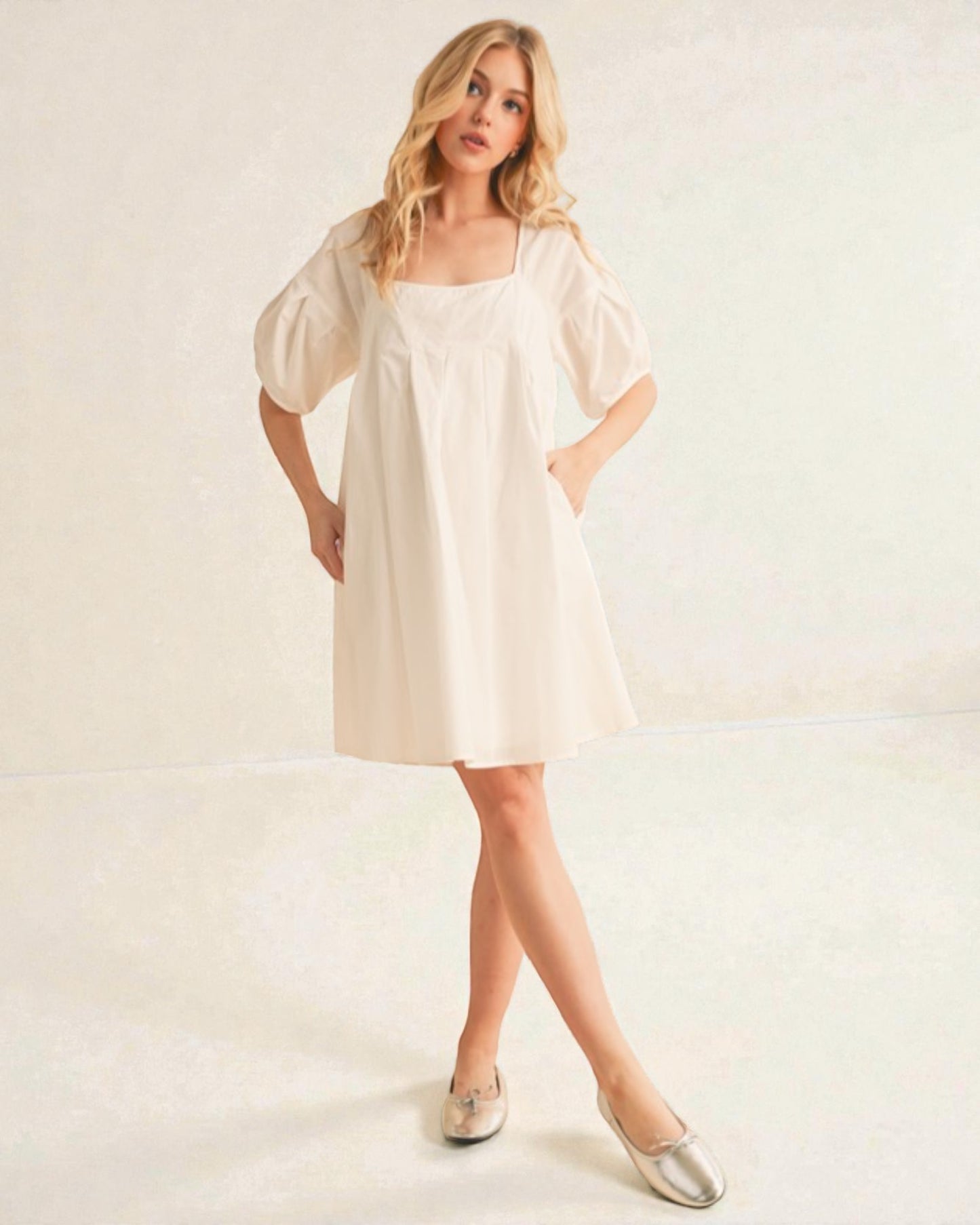 Woman wearing a white dress with puff sleeves on a plain background