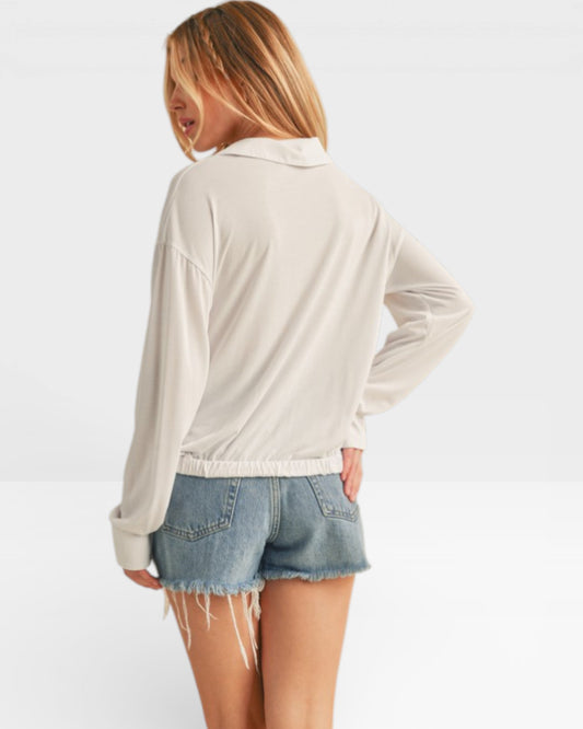 Woman wearing a beige long-sleeve top and denim shorts on a white background