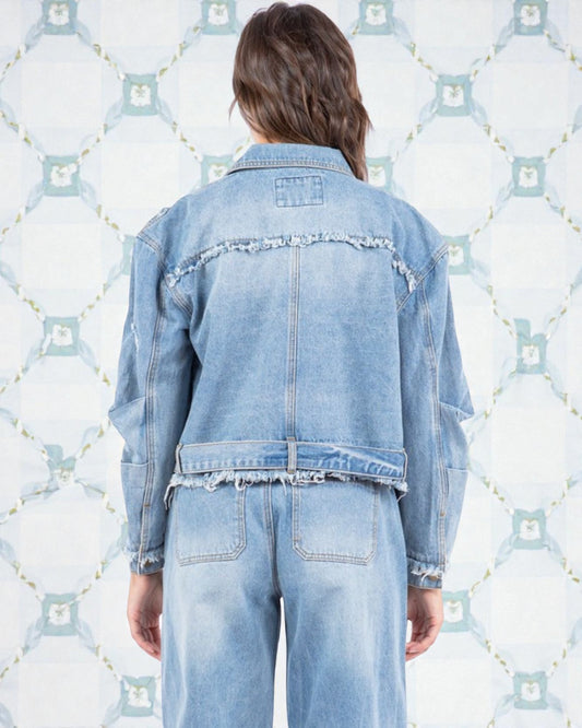 Person wearing a light blue denim jacket and jeans against a patterned background