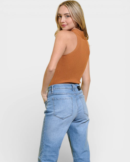 Woman wearing a rust-colored sleeveless top and light blue jeans on a white background