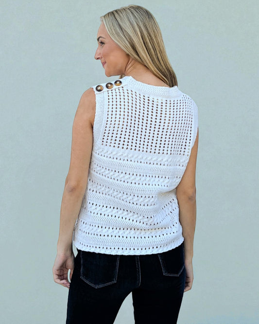 Woman wearing a white sleeveless crochet top against a light gray background