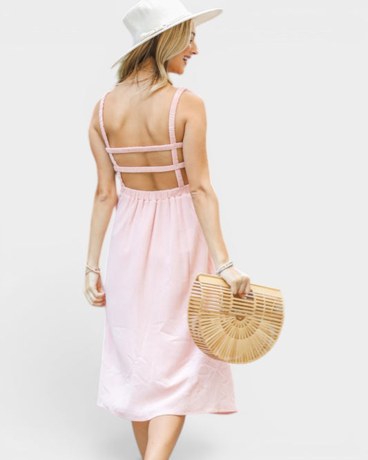 Woman wearing a pink dress with cut-out back, white hat, and holding a straw bag on a white background