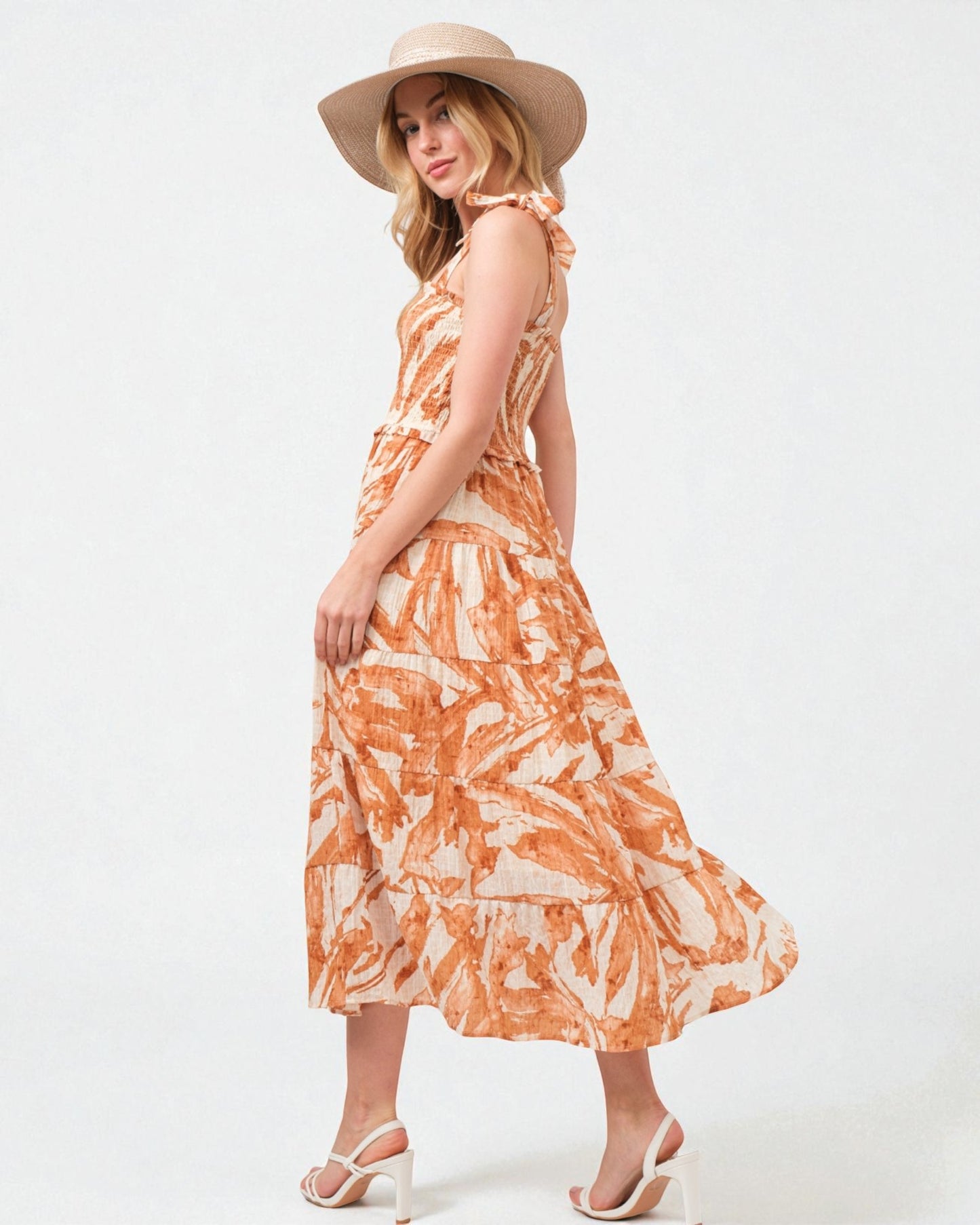 Woman wearing an orange and white patterned dress with a wide-brimmed hat on a white background