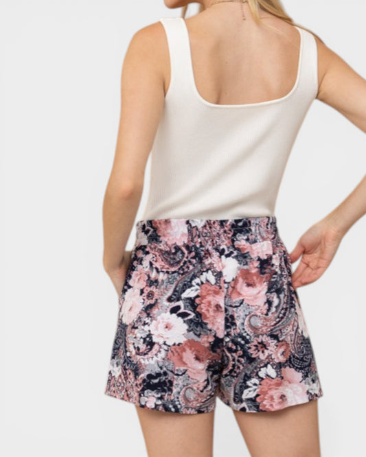 Person wearing a white tank top and floral shorts on a plain background