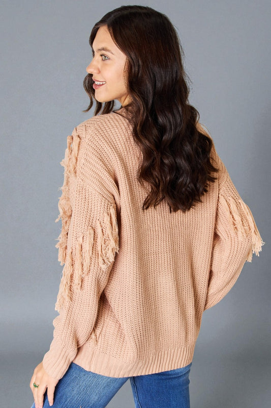 Woman wearing a beige knitted sweater with ruffled sleeves on a gray background