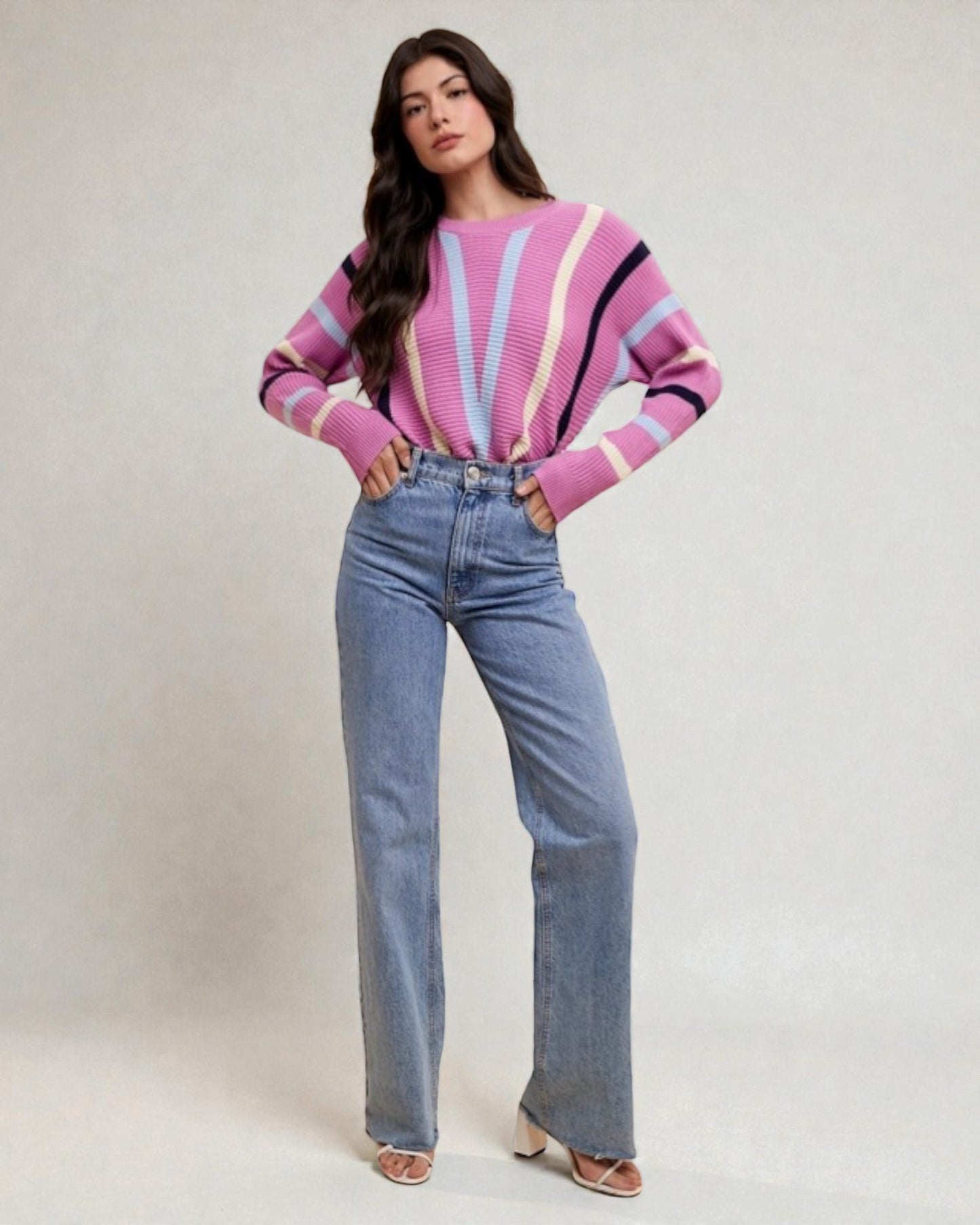 Woman wearing a pink and blue striped sweater and blue jeans on a white background