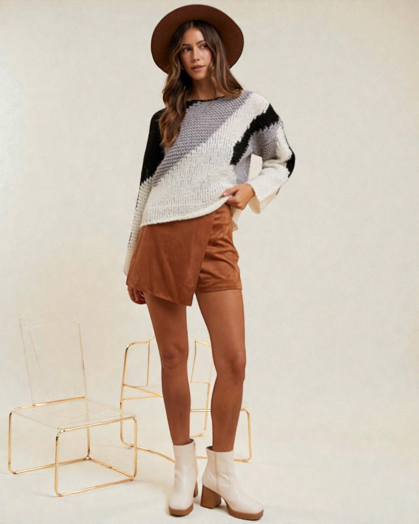 Woman wearing a patterned sweater, brown shorts, and white boots on a plain background
