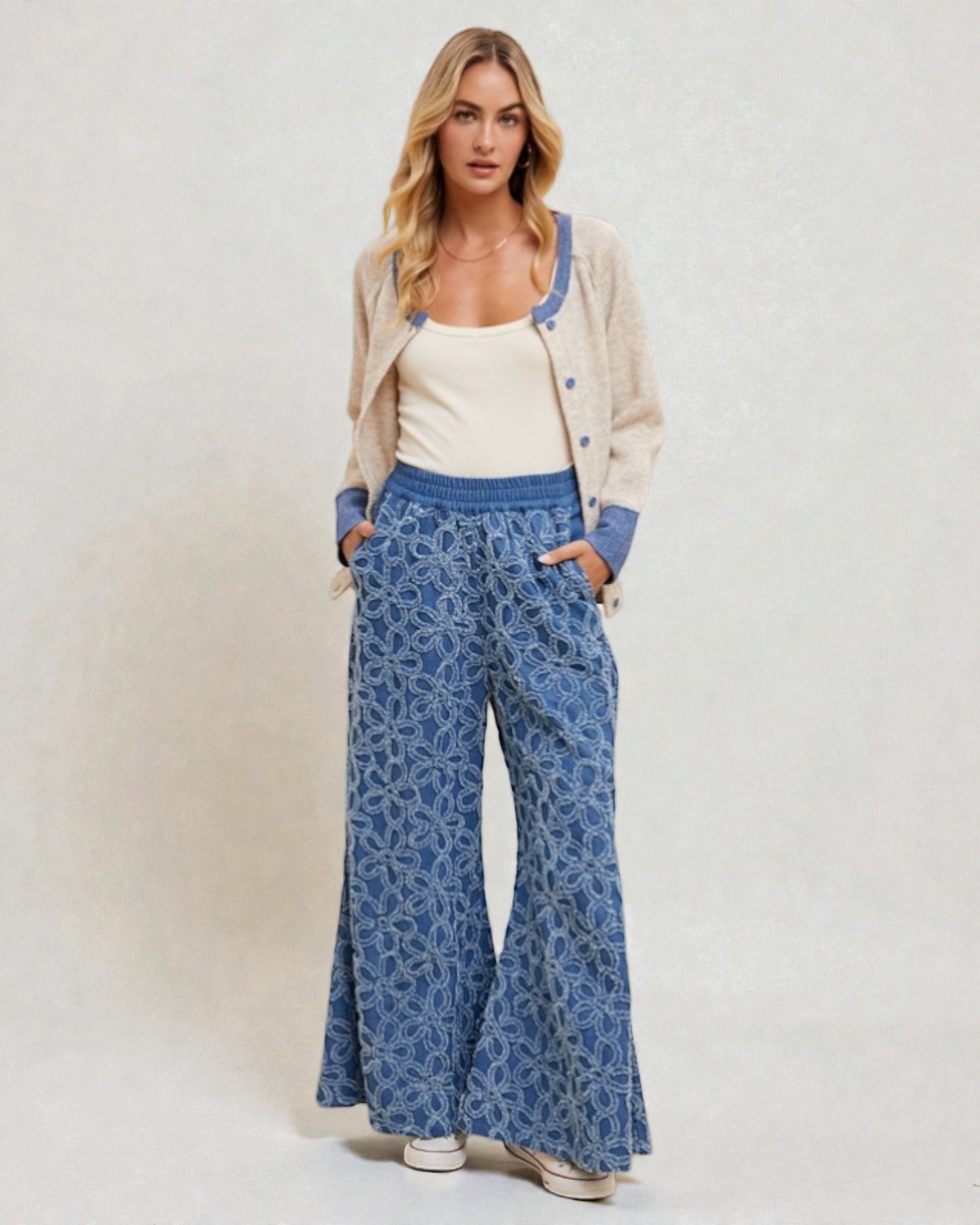 Woman wearing a beige cardigan, white top, and blue patterned pants on a plain background