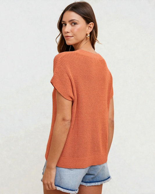 Woman wearing an orange knit top and denim shorts on a white background