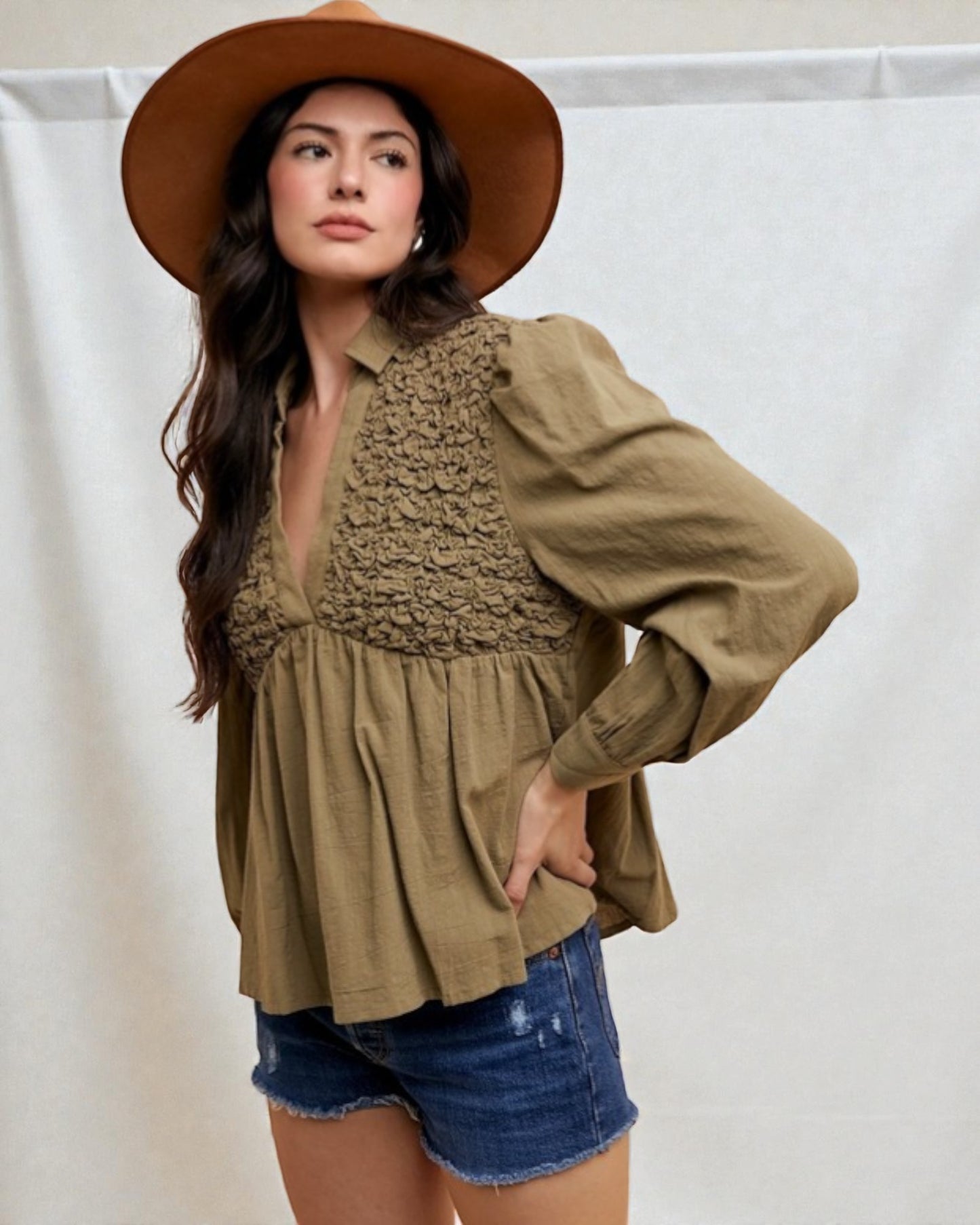 Woman wearing a brown hat, green top, and denim shorts against a white background