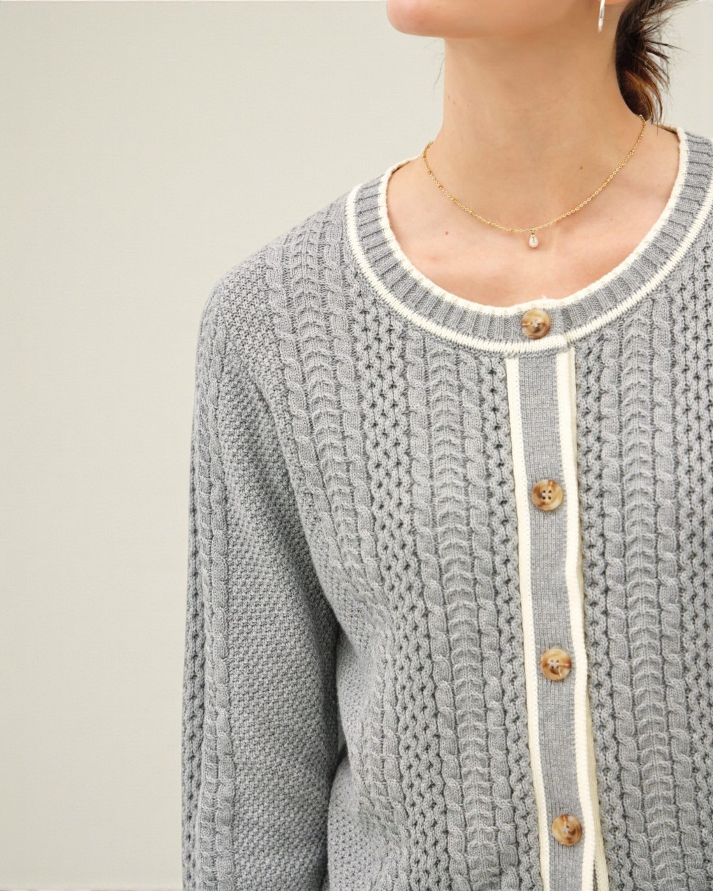 Gray knitted cardigan with white trim and gold buttons on a neutral background