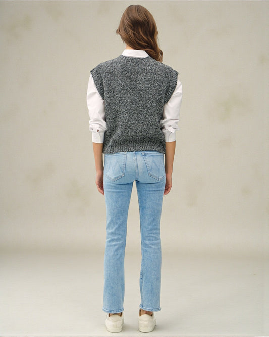 Person wearing a gray knitted vest, white shirt, and blue jeans on a plain background