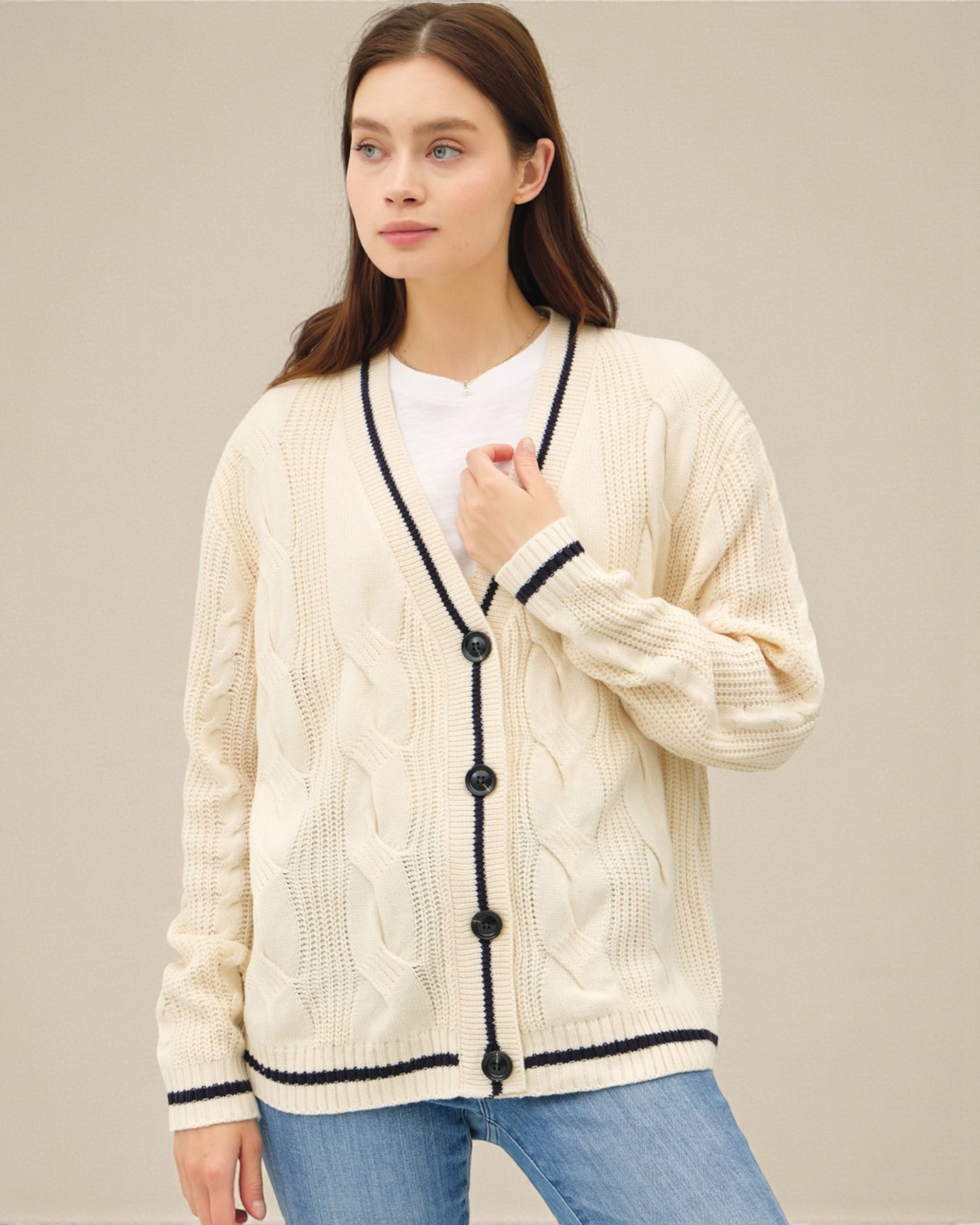 Woman wearing a cream cardigan with black buttons on a beige background
