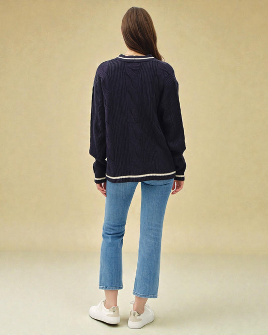 Person wearing a navy sweater and blue jeans on a beige background