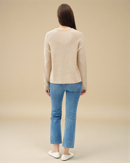 Person wearing a beige sweater and blue jeans on a beige background