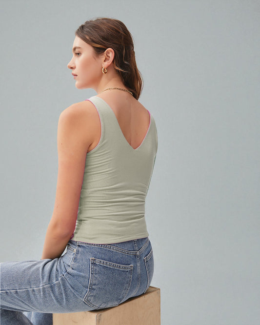 Woman wearing a light green tank top and blue jeans sitting on a box against a gray background