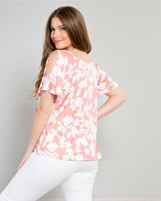 Woman wearing a pink floral blouse and white pants against a gray background