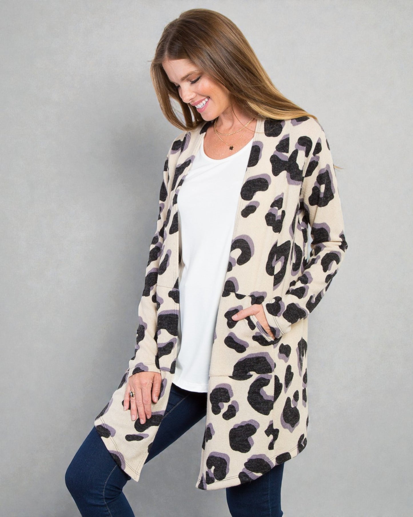 Woman wearing a leopard print cardigan over a white top and jeans on a gray background
