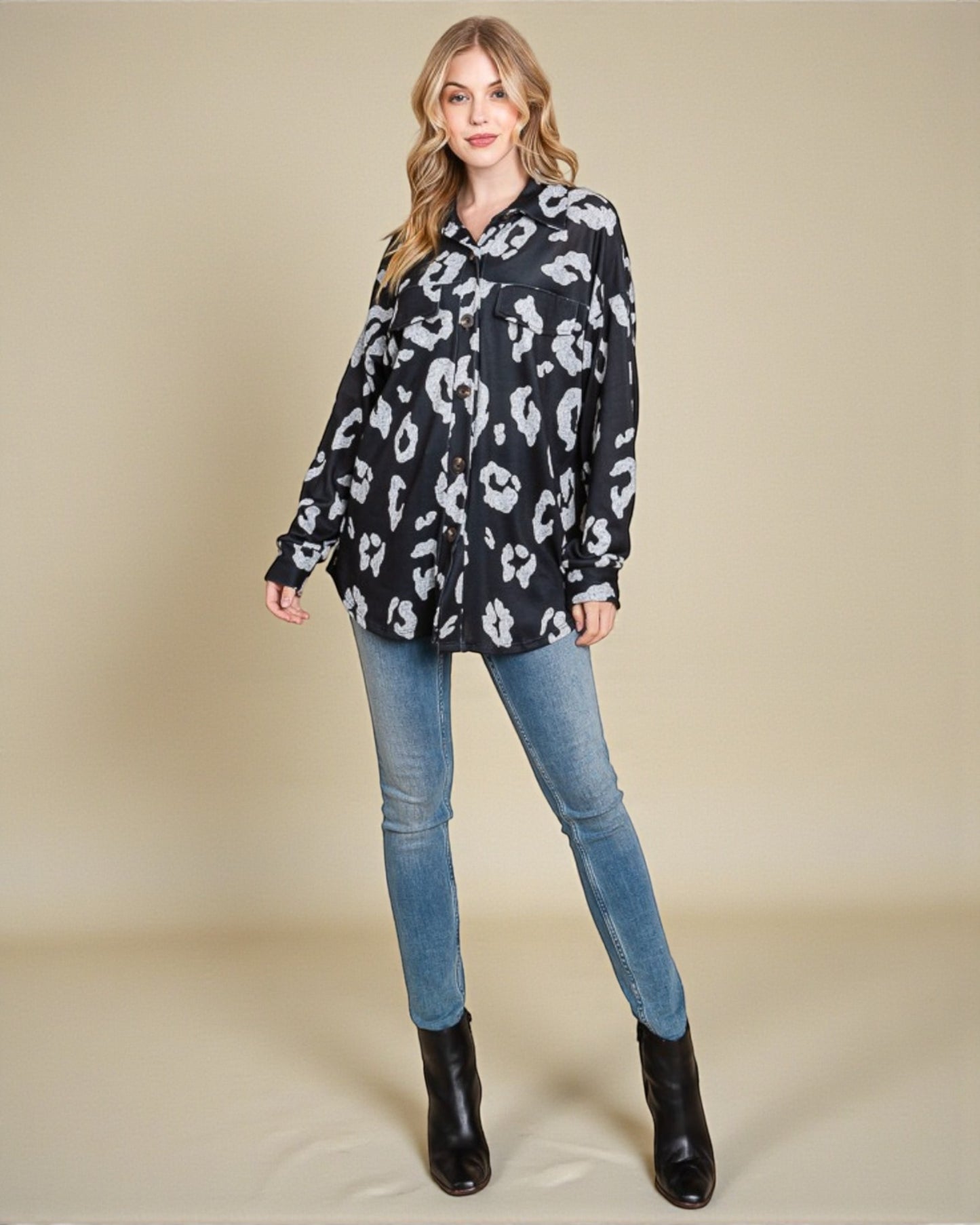 Woman wearing a black leopard print shirt, blue jeans, and black boots on a beige background