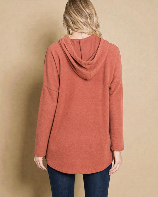 Person wearing a rust-colored hoodie against a beige background