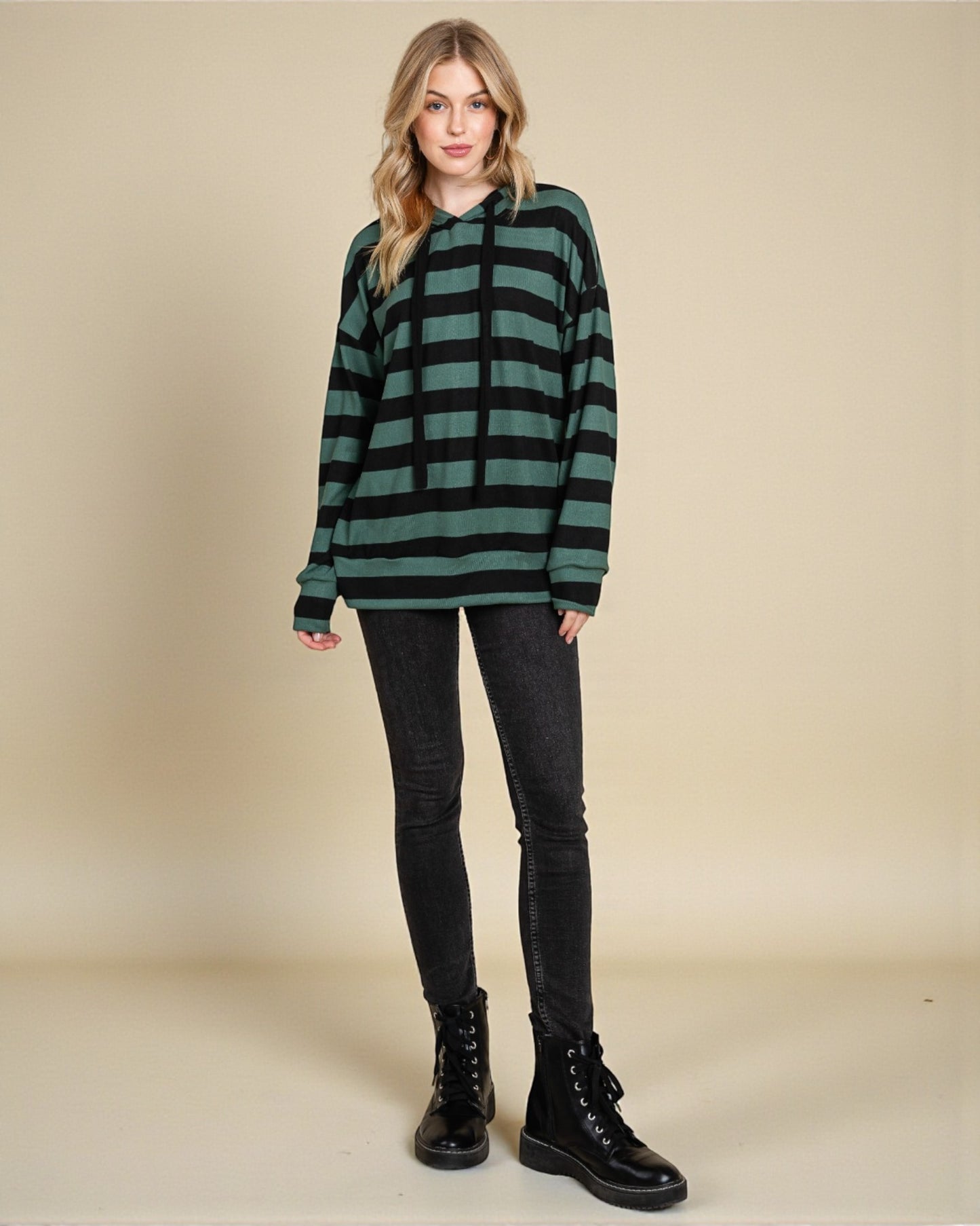 Woman wearing a green and black striped sweater with black pants and boots on a beige background