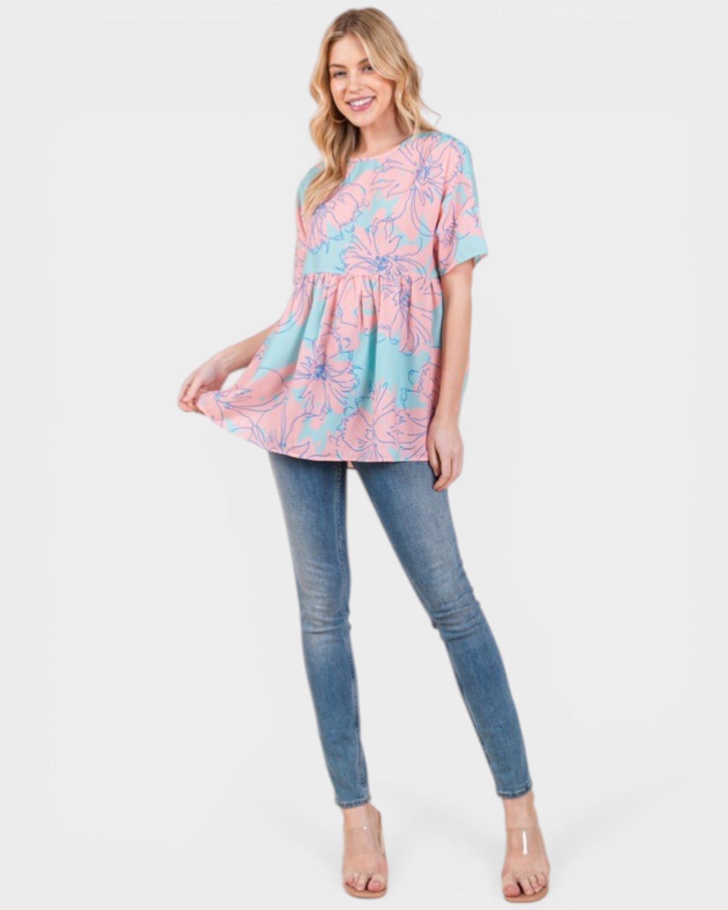 Woman wearing a pink and blue patterned top with blue jeans on a white background