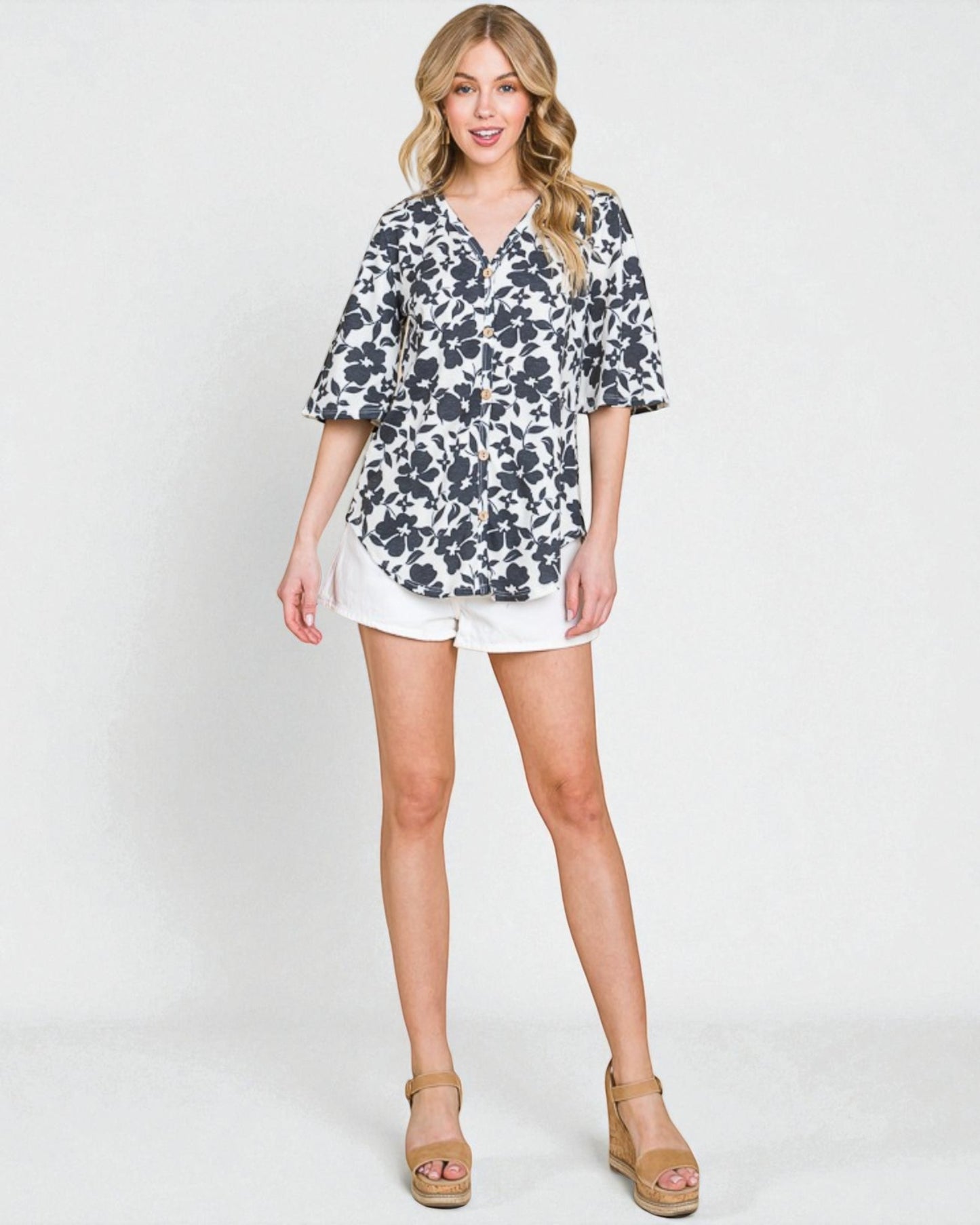 Woman wearing a floral blouse and white shorts on a plain background