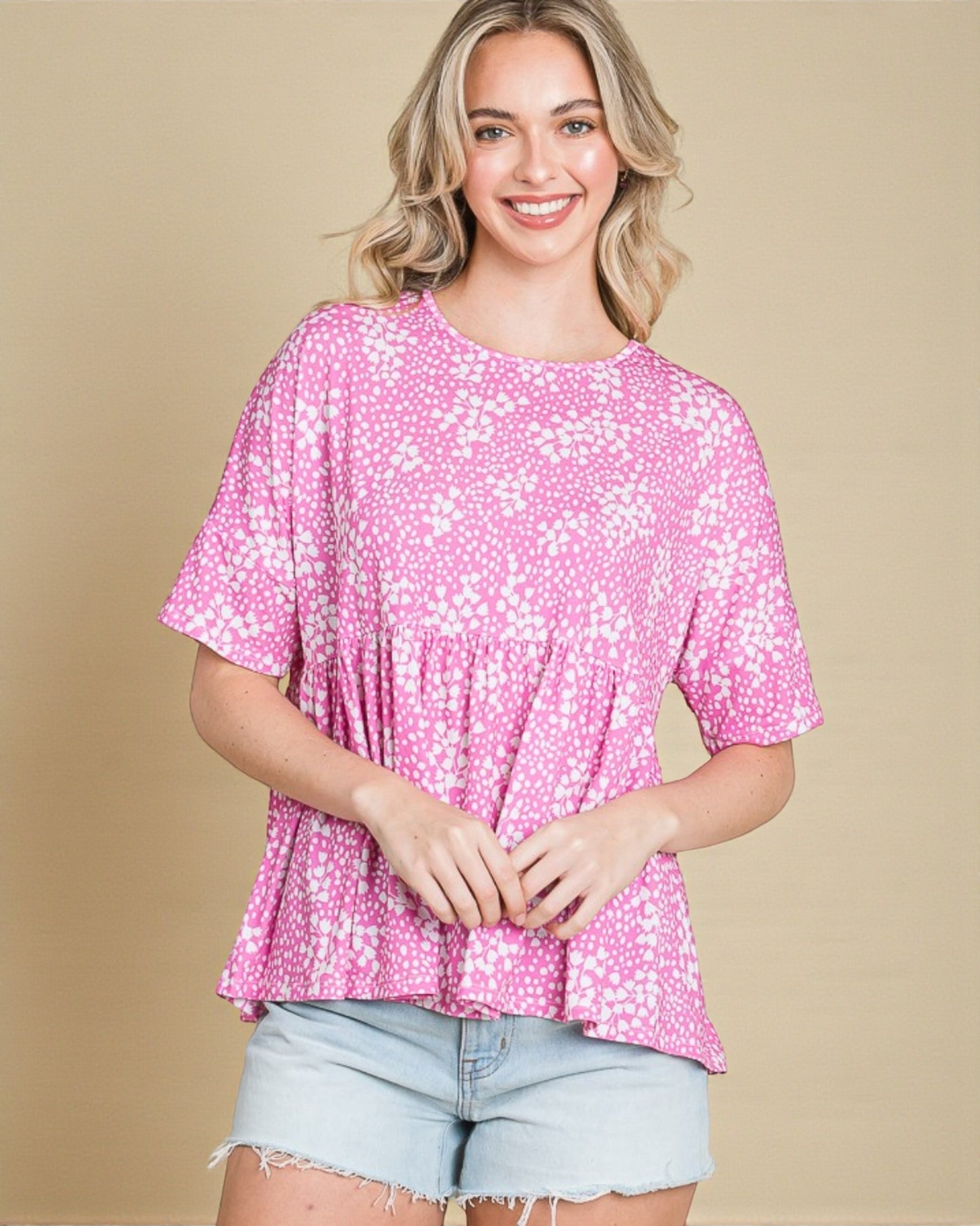 Woman wearing a pink floral blouse with denim shorts against a beige background