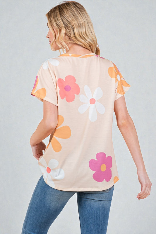 Woman wearing a beige t-shirt with colorful flower patterns on a plain background
