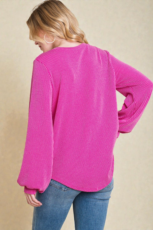Person wearing a bright pink ribbed sweater and blue jeans on a beige background
