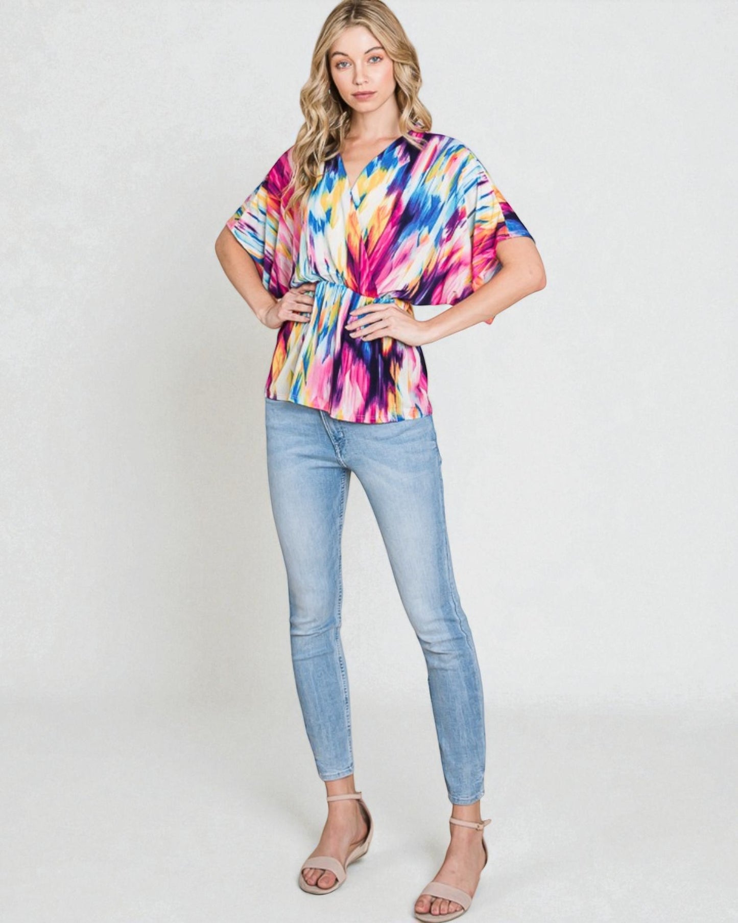 Woman wearing a colorful tie-dye top and light blue jeans on a white background