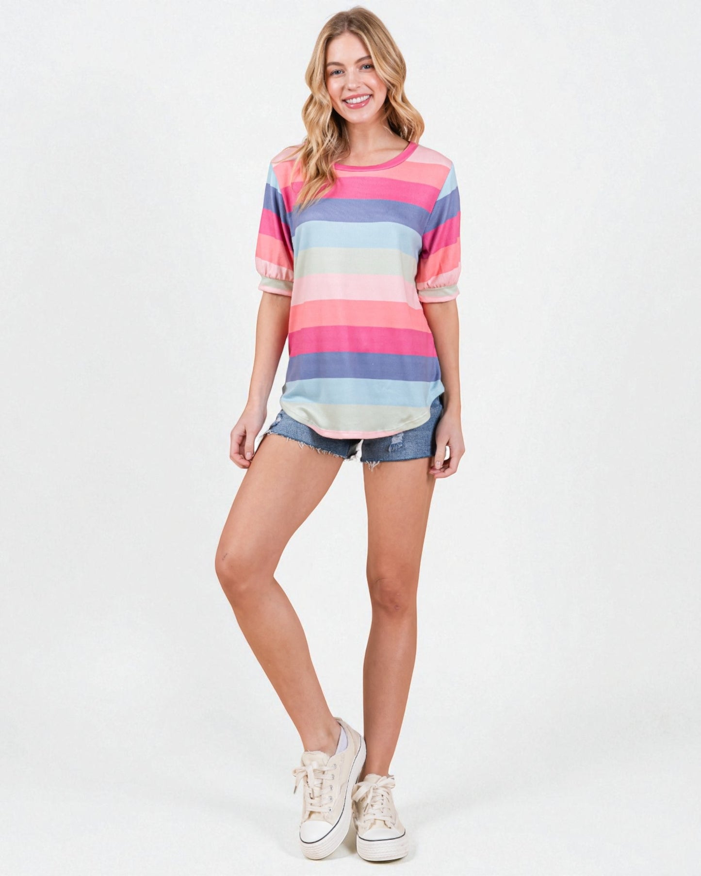Woman wearing a colorful striped shirt and denim shorts on a white background
