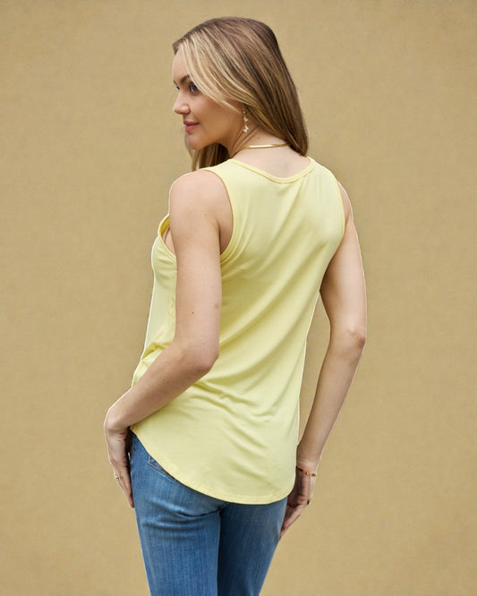 Woman wearing a yellow sleeveless top and blue jeans against a beige background