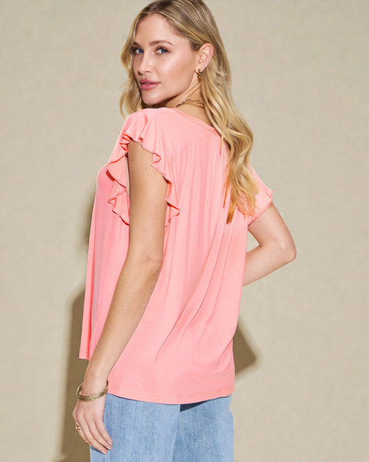 Woman wearing a pink blouse with ruffled sleeves against a beige background