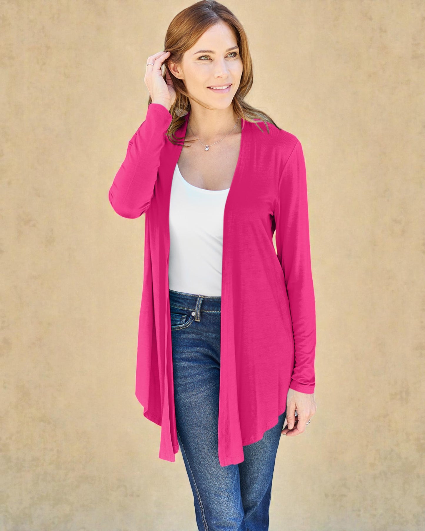 Woman wearing a bright pink cardigan over a white top and blue jeans on a beige background