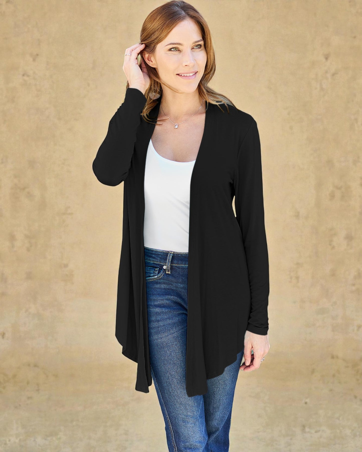 Woman wearing a black cardigan over a white top and blue jeans against a beige background