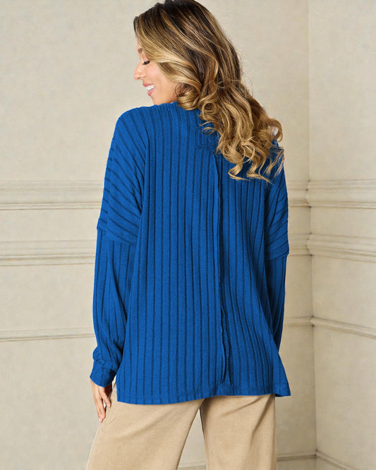 Woman wearing a blue ribbed sweater against a beige wall.