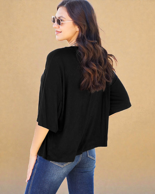 Woman wearing a black top and blue jeans against a beige background