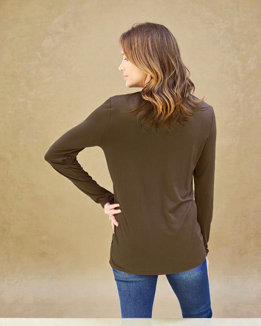 Woman wearing a brown long-sleeve top and blue jeans against a beige background