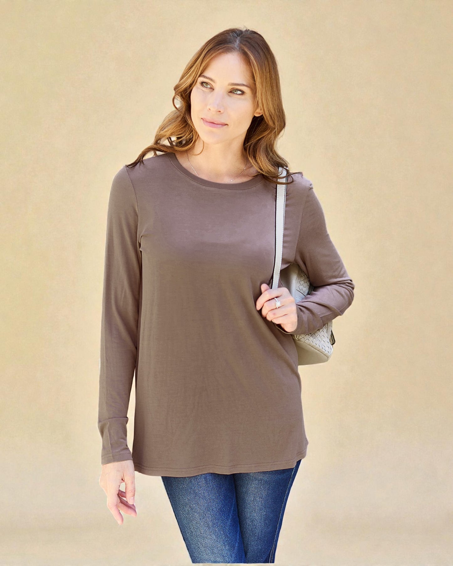 Woman wearing a brown long-sleeve top and blue jeans against a beige background