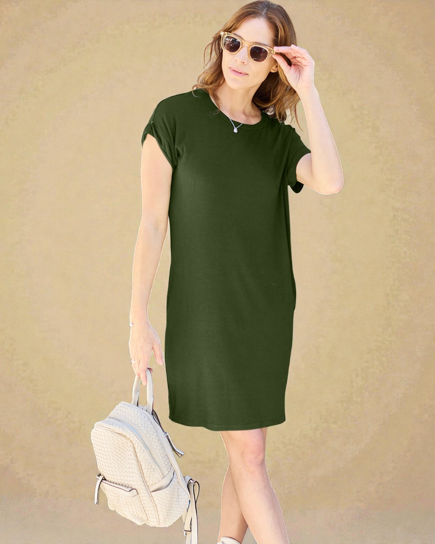 Woman wearing a green dress with sunglasses and a backpack against a beige background