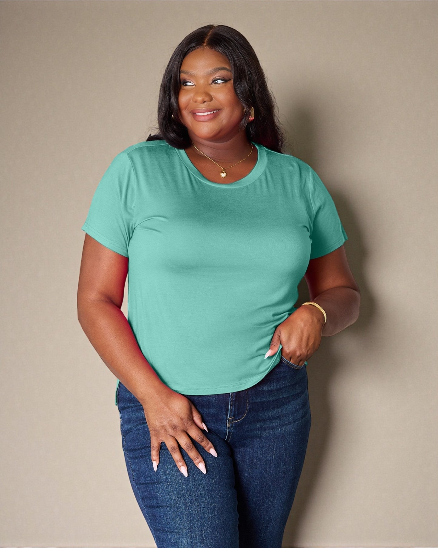 Woman wearing a teal t-shirt and blue jeans against a beige background