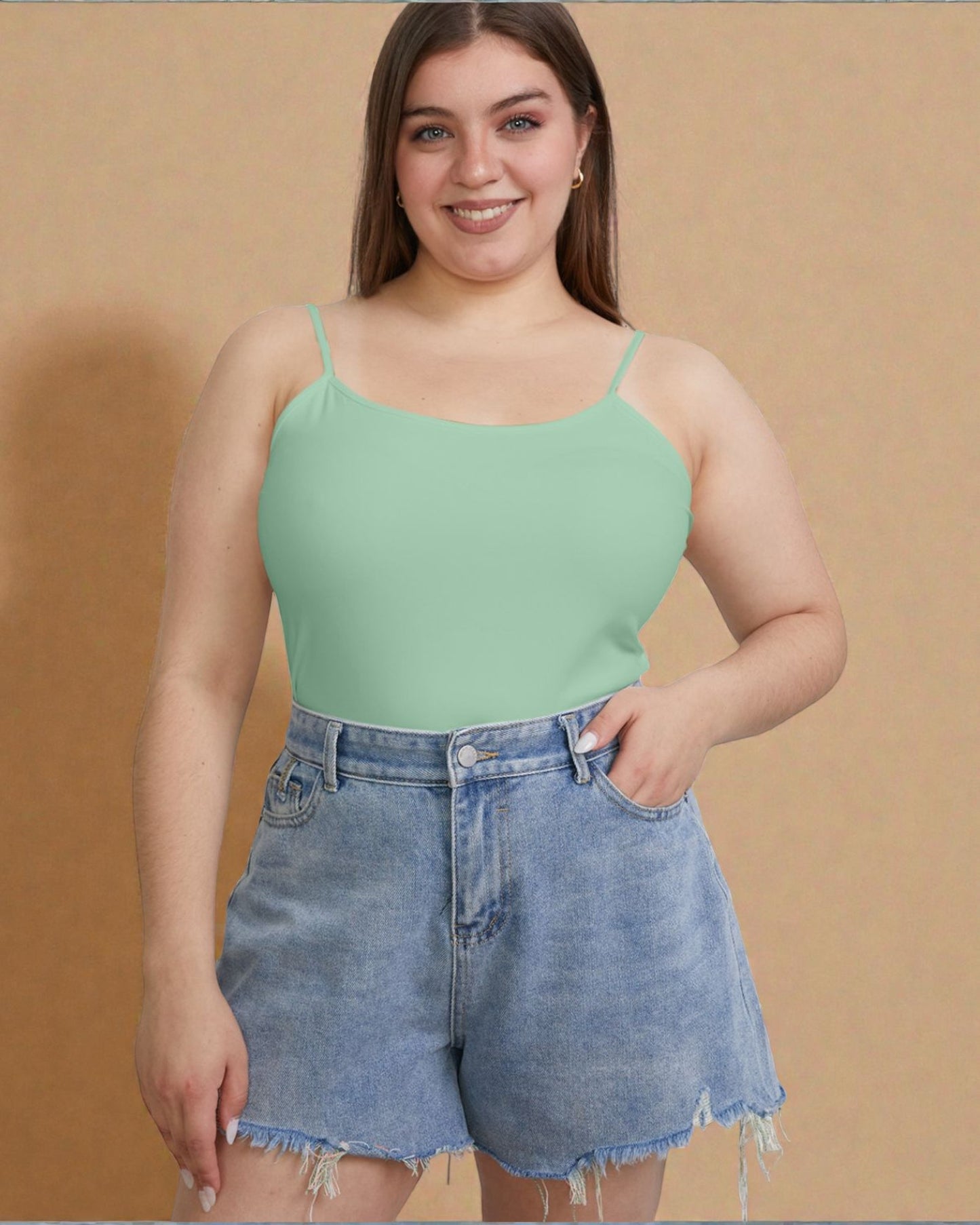 Woman wearing a green tank top and denim shorts against a beige background